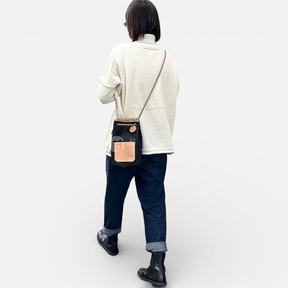 一個穿著白色高領毛衣和牛仔褲的女人，背著一個黑色尼龍束口袋斜背包，包包上有一個淺棕色皮革口袋。