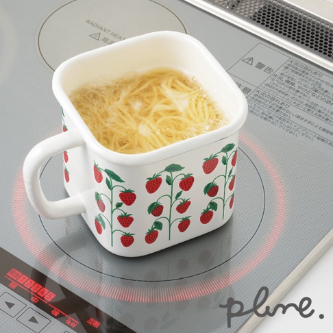一個白色琺瑯材質的方形保鮮罐，帶有提把，罐身印有紅色草莓和綠色葉子的圖案。保鮮罐內裝有正在烹煮的黃色麵條，置於電磁爐上，電磁爐顯示加熱指示。