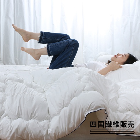 一位女子躺在白色無重力空氣被上，雙腳抬起，露出牛仔褲褲腳。被子呈現蓬鬆的白色，表面有縫線紋路。