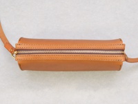 職人手作皮革Organ極簡風拉鍊單肩包，採用天然棕色皮革製作，搭配金色拉鍊和皮革肩帶。包身呈圓筒狀，線條簡潔流暢，邊緣有精細的縫線裝飾。