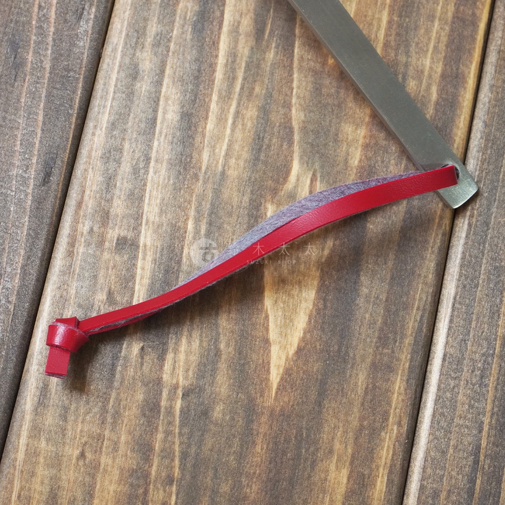 不鏽鋼萬用湯勺，勺柄處有紅色皮革與灰色織帶裝飾，皮革末端打結。