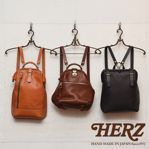 三款職人手作皮革後背包，分別為淺棕色、咖啡色及黑色。前兩款為圓潤造型，後一款為方正設計，皆配有可調節的皮革肩帶和金屬扣環。