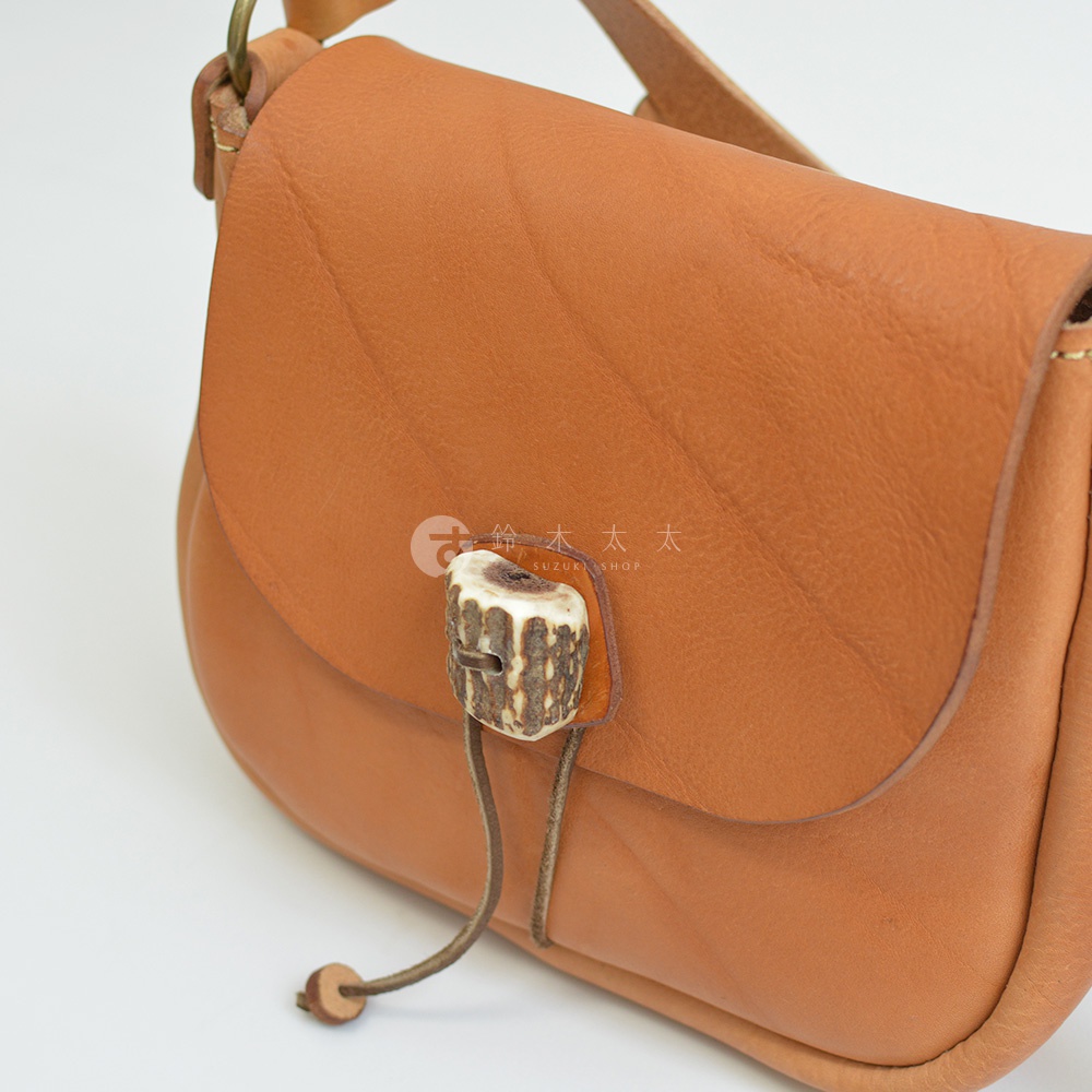 棕褐色皮革製成的職人手作斜背包，具有鹿角造型的扣環和皮革繩束帶。