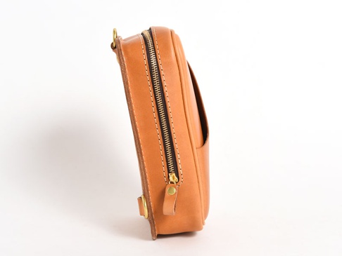 淺棕色植鞣皮革製成的直立型斜背包，側面展示，配有金色拉鍊和縫線細節，以及可拆卸的皮革肩帶。