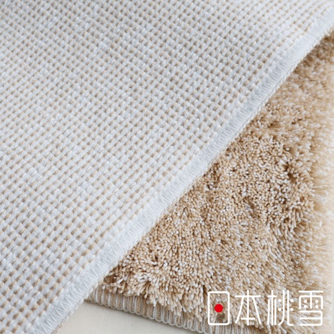 兩塊觸感柔軟的淺米色和米黃色浴墊，其中一塊有細膩的格子圖案，另一塊則有濃密的毛圈，右下角有「日本桃雪」的白色字樣和紅色圓點標誌。