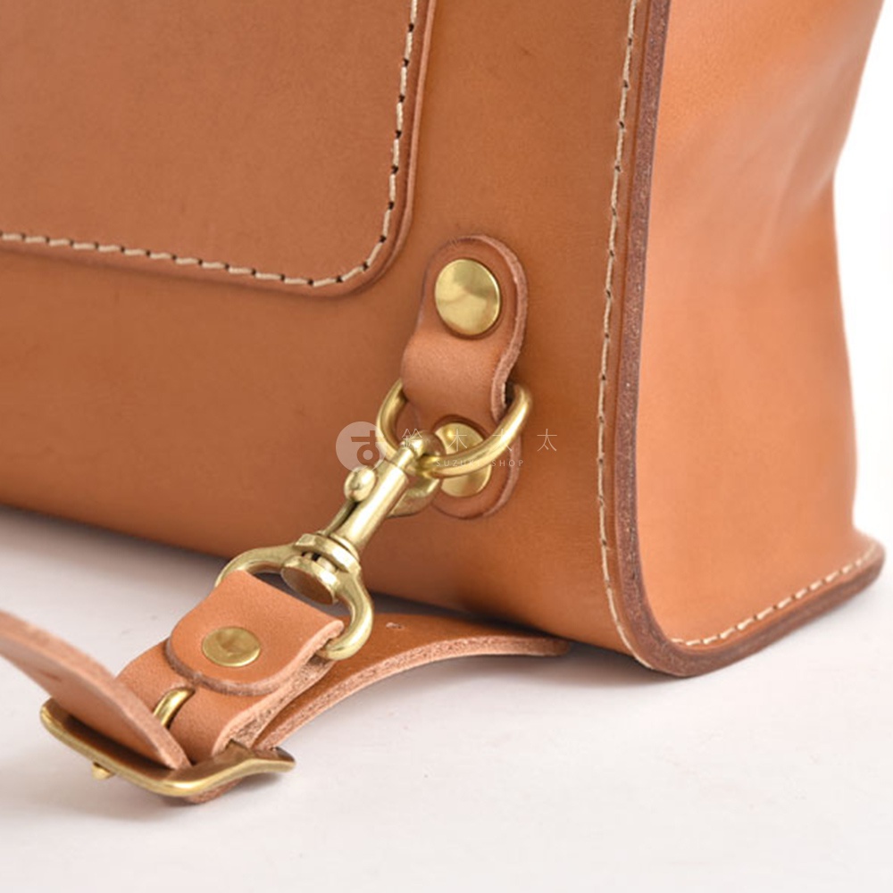 原色皮革迷你後背包，設有金色金屬釦環與鉤扣，搭配米白色縫線，展現簡潔質感。