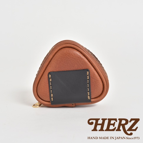 職人手作皮革小物收納包，造型為三角飯糰，採用棕色皮革製作，前方有黑色皮革裝飾片，以明線縫合，附有金色拉鍊。