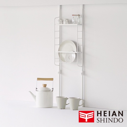 白色廚衛兩用收納籃架，附有兩層置物架，上方擺放杯子和玻璃罐，下方置物籃內有盤子和杯盤。左側有一白色茶壺，搭配木質提把，並有兩個淺灰色馬克杯。