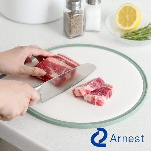 圓形白色抗菌料理砧板，邊緣為淺綠色，上面放著正在被切割的生肉塊，以及兩塊已切好的肉。