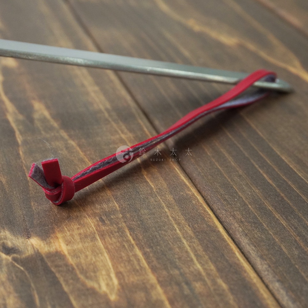 不鏽鋼萬用瀝水湯勺特寫，湯勺為金屬材質，勺柄末端繫有紅色皮革掛繩，掛繩末端打結固定。