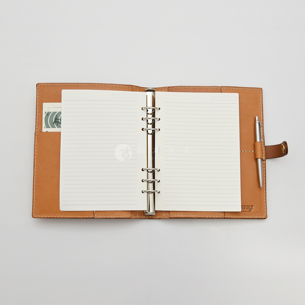 職人手作皮革A5手帳，打開狀態，內頁為橫線筆記紙，右側有筆插固定一支銀色金屬筆，左側有卡片插槽，封面為淺棕色皮革。