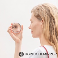 一位金髮女子手持一個約 7 公分直徑的銀色金屬圓形化妝鏡，鏡中映照出她半張臉。