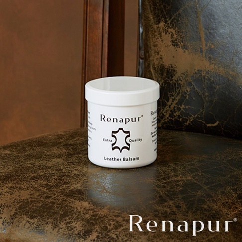 白色圓形罐裝的 Renapur 皮革保養油，罐身印有品牌名稱、皮革圖標、「Extra Quality」字樣以及「Leather Balsam」產品名稱。罐子放置於深棕色紋理皮革表面上。