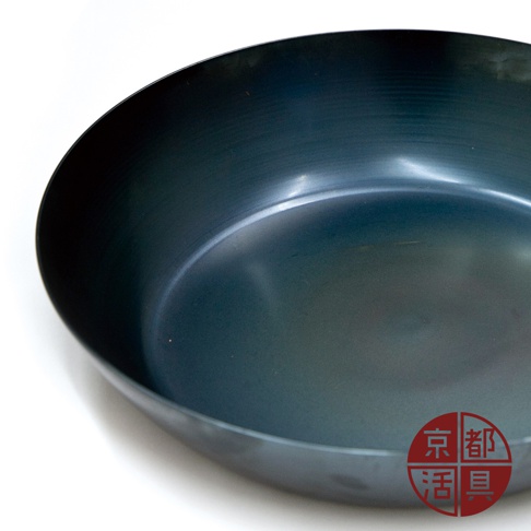 一個28公分的深藍色無塗層平底鐵鍋，鍋身呈現霧面質感，鍋緣圓潤，底部光滑。右下角有紅色圓形標誌，印有「京都」和「活具」字樣。