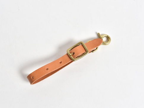 淺棕色皮革製成的吊掛帶，配有黃銅色方形環和鉤扣，可調節長度，設計簡約。