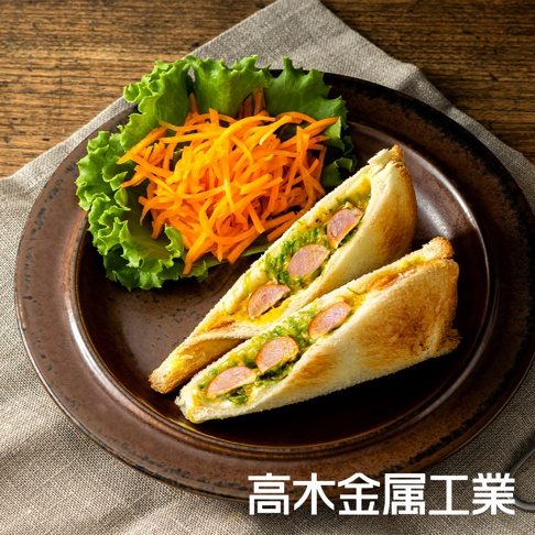 兩片烤過的口袋吐司，內夾香腸片與綠色醬料，搭配一旁的新鮮生菜和刨絲紅蘿蔔，盛裝於深棕色圓盤中。