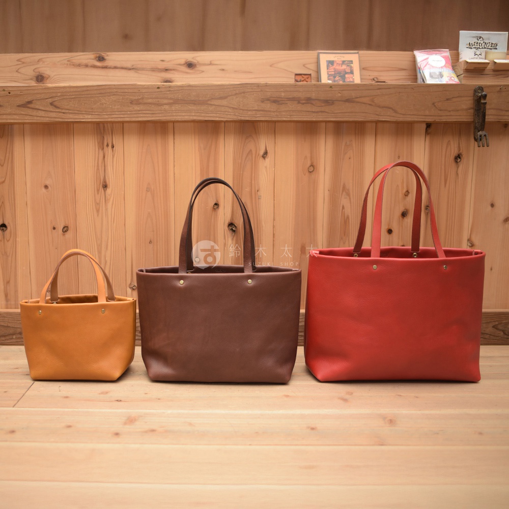 三款不同尺寸的皮革托特包，分別為淺棕色、深棕色與紅色，皆為簡約設計、手提款式。