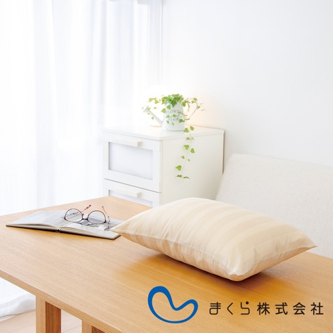 淺米色條紋純棉枕套的柔彈午睡枕，置於木桌上，旁邊有眼鏡和打開的書本。