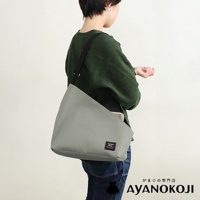 一名女子身穿綠色毛衣，斜揹著一個灰色方形口金單肩包，包上有品牌的黑色標籤，背景為純白色。