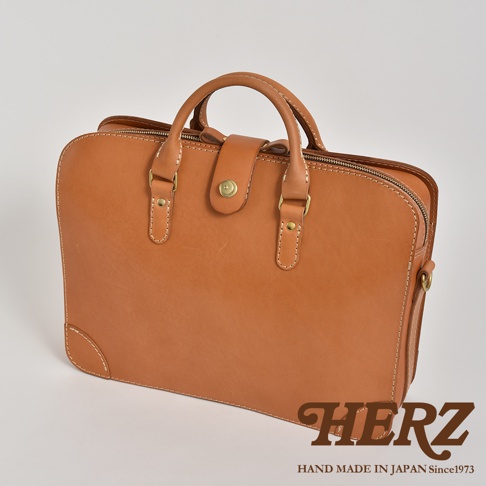 淺棕色皮革製成的手提公事包，具備雙提把、銅扣開合主隔層，以及拉鍊側袋。包款設計簡約，適合商務場合。