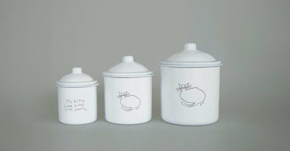 三個不同尺寸的白色琺瑯儲物罐，帶有蓋子，罐身上繪有簡約的貓咪圖案或手寫文字「My kitty likes to play with yarn.」。