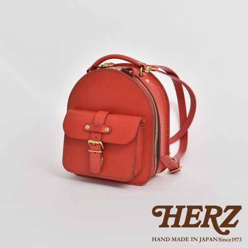 職人手作皮革迷你後背包，鮮紅色，正面有翻蓋口袋及皮帶扣，兩側有拉鍊，附有可調節的皮革肩帶。