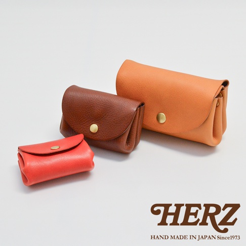 三款皮革零錢包，分別為鮮紅色、棕色和橘色，皆為職人手作，設計簡約，帶有金色釦子。