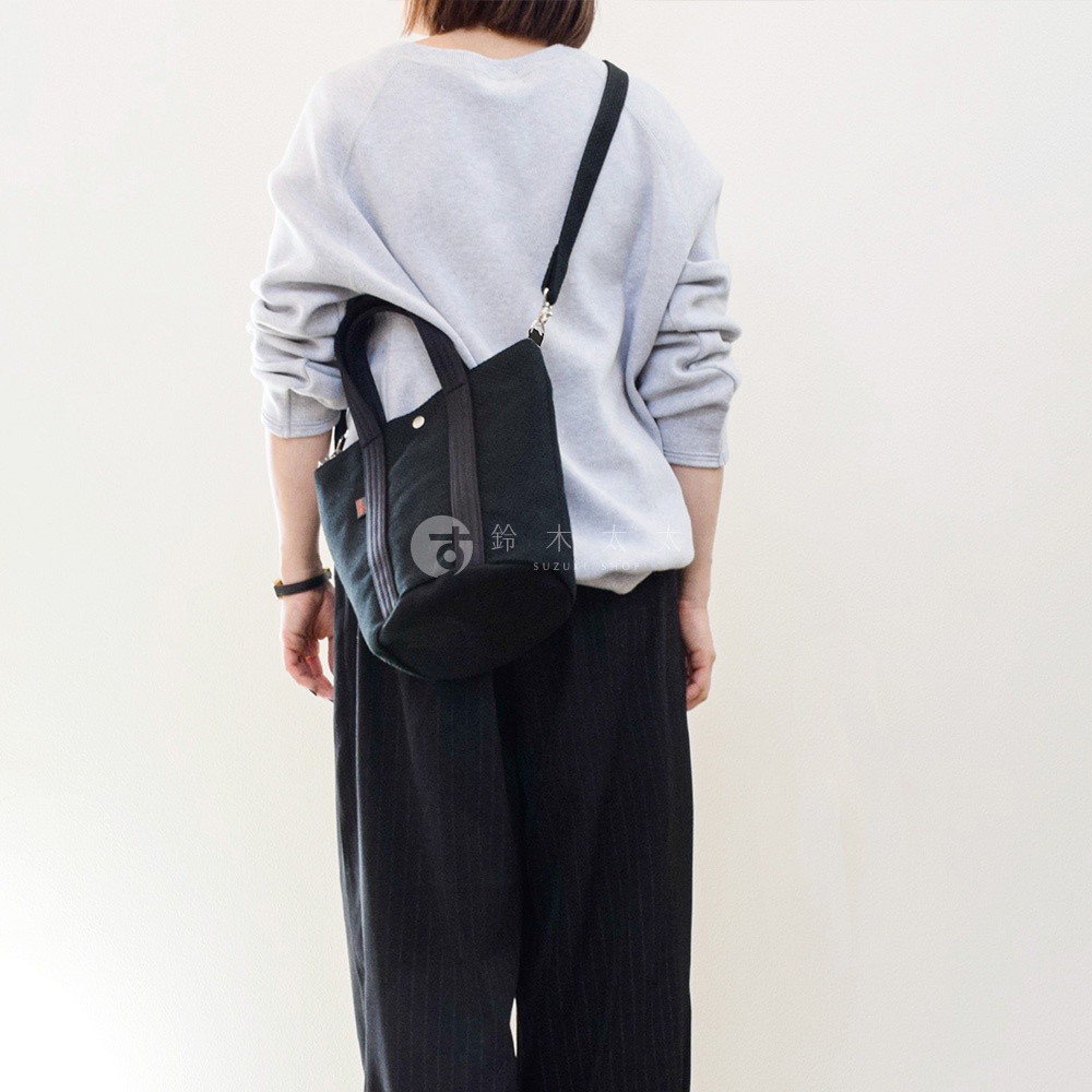 一位女士背著黑色三河木綿刺子織兩用水桶包，包包上有品牌標誌。