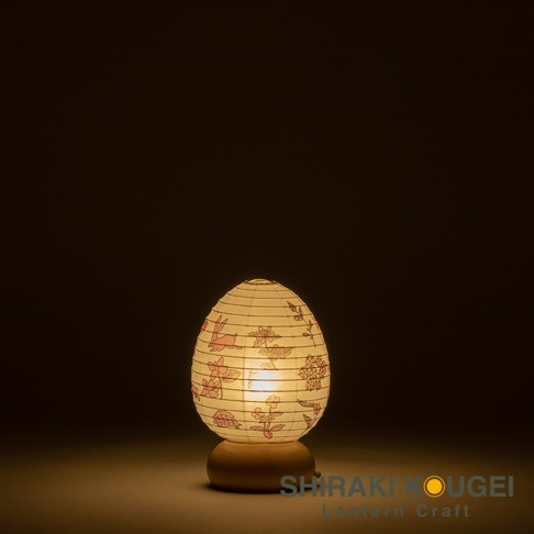 日式雞蛋造型紙燈，燈罩為白色，印有粉色兔子和花卉圖案，下方為木質底座，燈光溫暖。