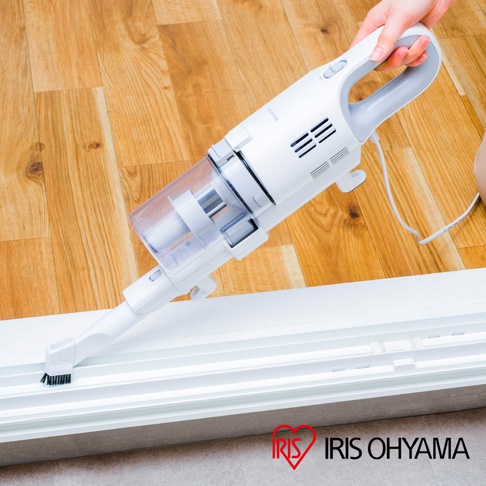 白色與灰色手持式有線吸塵器，配備透明集塵筒，正使用刷頭清潔白色窗框。