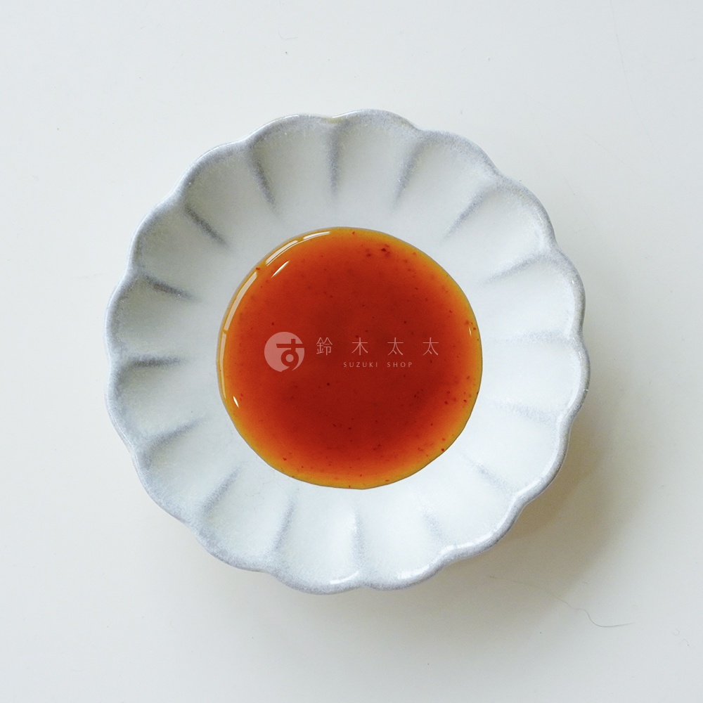 俯視視角拍攝的白色荷花造型小碟子，中央盛放著色澤紅潤濃郁的調味醬，醬料表面隱約可見細小的香料顆粒，碟子中心印有鈴木太太 SUZUKI SHOP 的品牌商標與日文字樣，整體畫面呈現簡潔乾淨的質感。