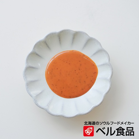 北海道芝麻擔擔風味沙拉醬，裝在帶有扇形邊緣的白色小盤中，醬料呈現橘紅色，上面點綴著細小的深色顆粒。下方有日文標誌「北海道のソウルフードメーカー ベル食品」。