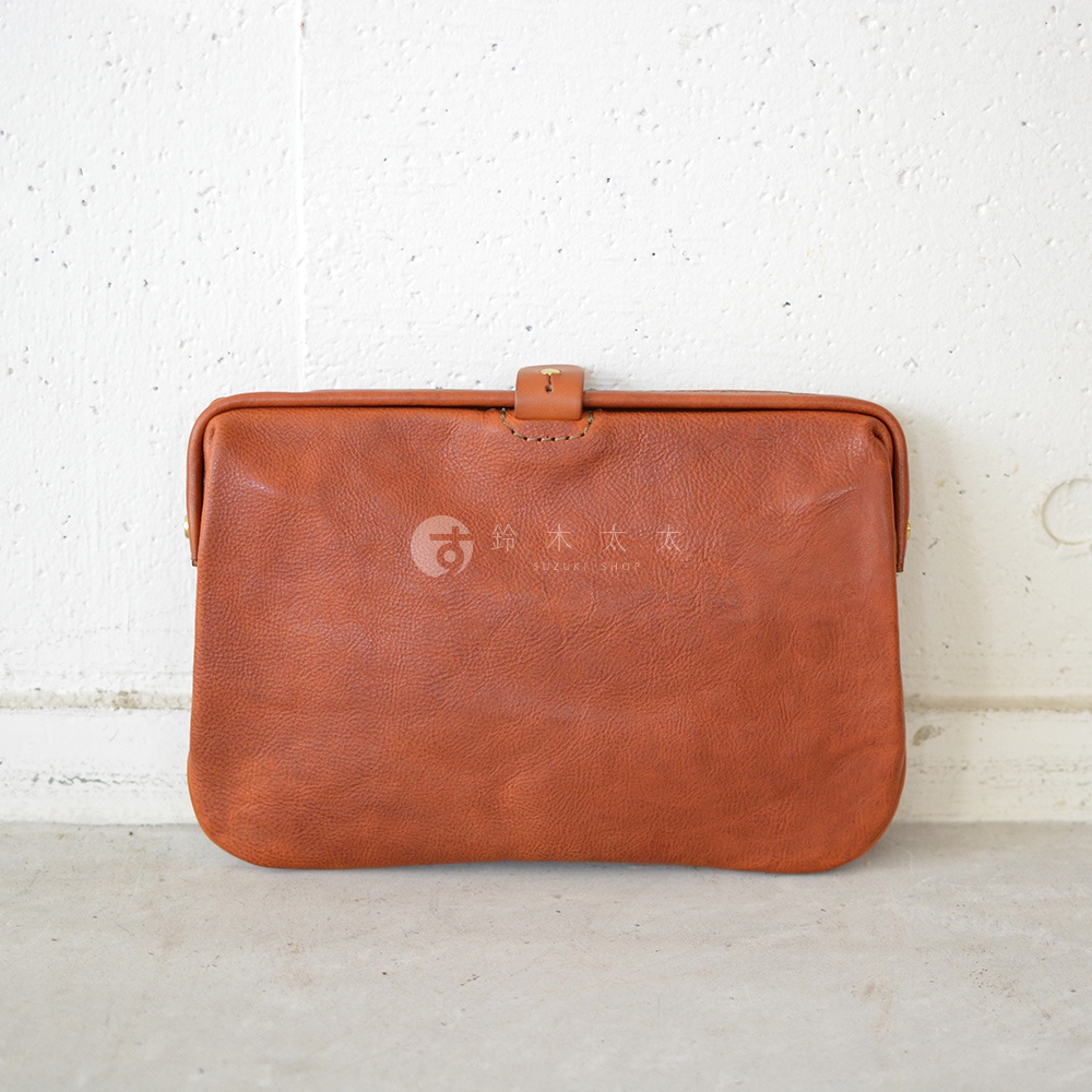 職人手作皮革Organ手拿包，呈現溫潤的棕褐色，材質為柔軟的真皮，包身上有品牌標誌，並以金屬扣環開合。