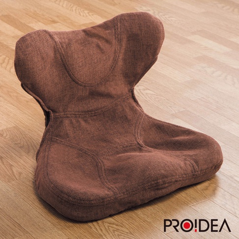 棕色布質馬鞍型正姿座墊，具有人體工學設計，能支撐臀部與背部，表面紋理清晰，置於淺木紋地板上。