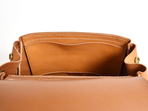 職人手作皮革屋瓦風迷你後背包 (R-6) 內部，展示了淺棕色皮革材質，有兩個開放式隔層，邊緣有精緻縫線，並可見金屬釦件。