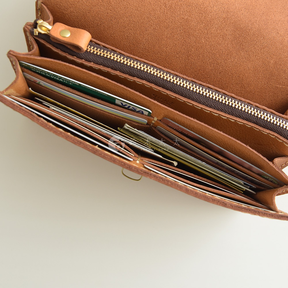 棕色皮革手風琴式長夾，內有多個卡槽，塞滿信用卡、現金和收據。其內襯為柔軟的皮革，並配有金色拉鍊和皮革拉頭。
