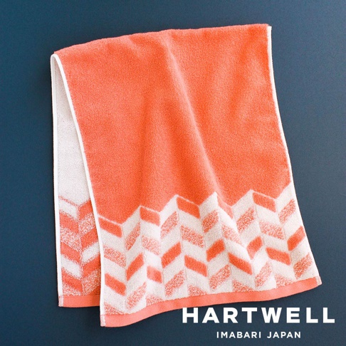 珊瑚橘色今治毛巾，飾有白色鋸齒狀傳統紋樣，質地柔軟，適合居家或旅行使用。