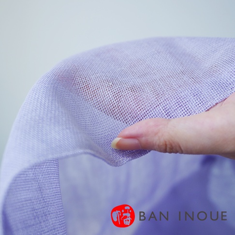 一隻手正輕柔地抓握著淡紫色、網狀織紋的織品，展現其細緻的紋理，下方可見品牌標誌。