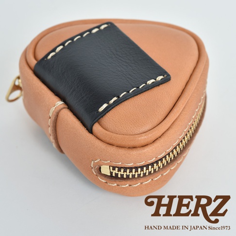 職人手作皮革小物收納包，呈現三角飯糰造型，主體為淺棕色皮革，頂部裝飾有黑色皮革片，以米白色縫線裝飾。