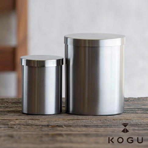 兩個日製18-8不鏽鋼圓柱形儲存罐，帶有銀色金屬光澤，一個較小，一個較大，皆配有圓形頂蓋，置於木質桌面。