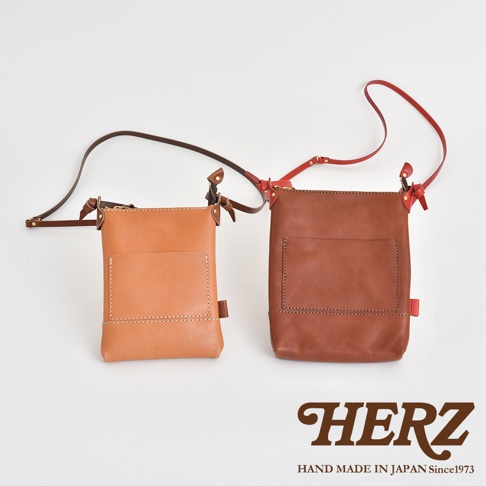 兩款職人手作皮革直式隨身單肩包，一款為淺棕色，另一款為深棕色，均採用光滑皮革材質，配有同色系或對比色的細長肩帶，包身正面有方形貼袋設計，並以白色車線縫合。