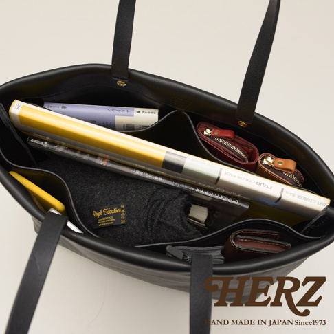 黑色皮革極簡托特包，內部可見書本、雜誌、手機，以及一個紅色和一個棕色的皮質零錢包。