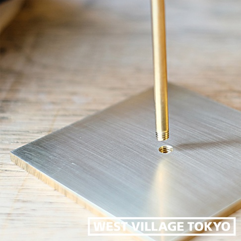 黃銅圓柱狀燈架與銀色金屬方形底座，底座表面有細緻的髮絲紋，圓柱底部有螺紋，對應底座上的螺孔，準備組裝。