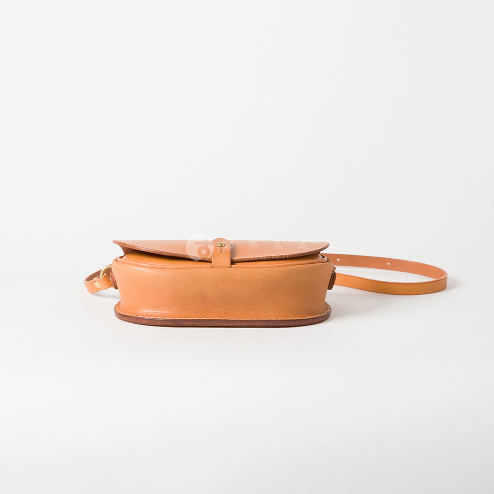 職人手作皮革迷你馬鞍包，淺棕色，圓潤弧形設計，翻蓋處有金屬釦環，搭配同色皮革背帶。