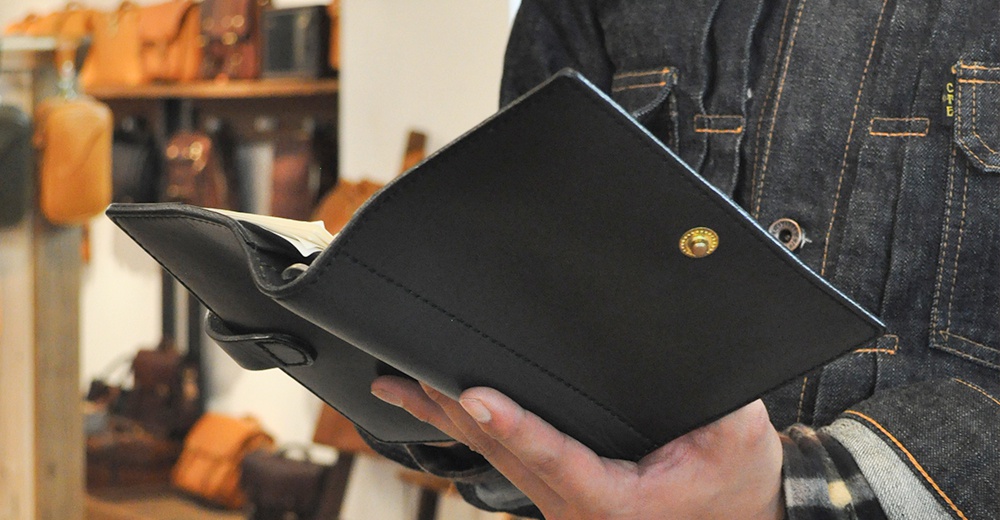 黑色皮革手帳/記事本書套，有著精緻的車縫線和金屬按扣。