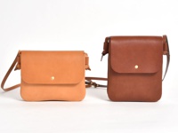 兩款職人手作皮革橫式隨行袋，一款為淺棕色，另一款為深棕色。皆為真皮材質，設計簡約，配有翻蓋式開口和金色金屬釦。