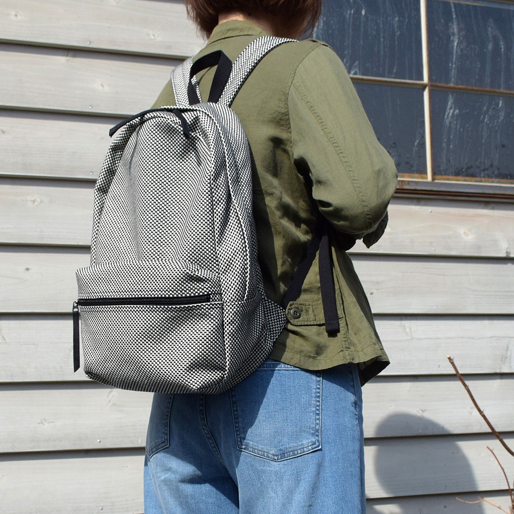 一款三河木綿刺子織後背包，採用黑白格紋圖案，配有黑色拉鍊和肩帶，整體造型簡約。