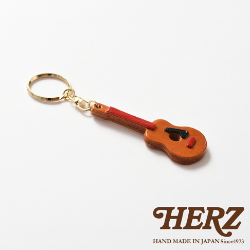 職人手作皮革吉他造型鑰匙圈，主體為棕色皮革，吉他琴頸為紅色，黑色與紅色點綴。