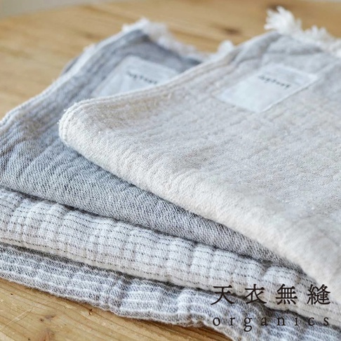 三條堆疊的 HEATHER 有機混紡棉浴巾，呈現條紋紋理，顏色從淺灰到米白色，邊緣有流蘇細節。