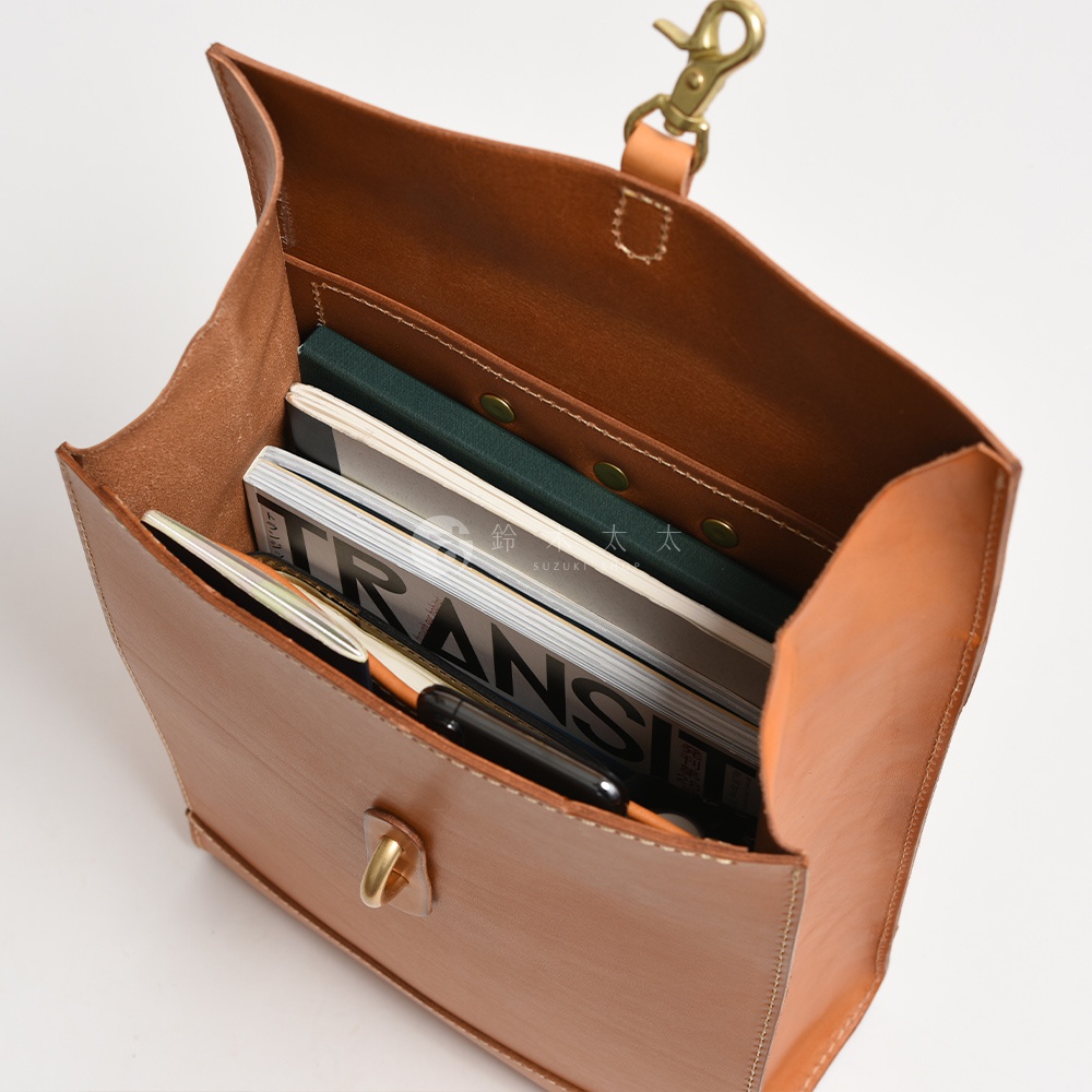 職人手作皮革紙袋風後背包，淺棕色，皮革材質，內部裝有雜誌和筆。